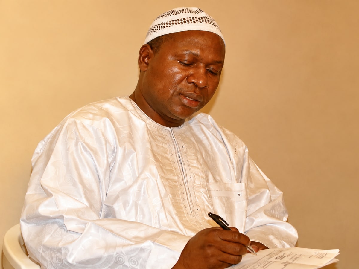 Maitre TAYA, en boubou blanc, prenant des notes dans son cabinet